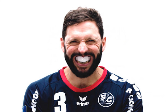Ein Handballspieler zeigt seinen Mundschutz