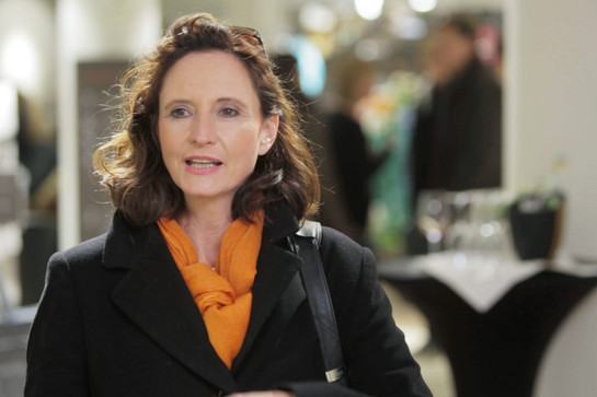 Eine Frau trägt einen orangenen Schal und einen schwarzen Mantel