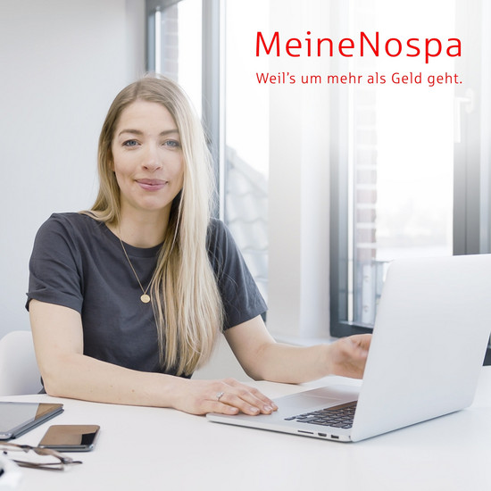 Eine blonde Frau sitzt vor einem Laptop und schaut in die Kamera