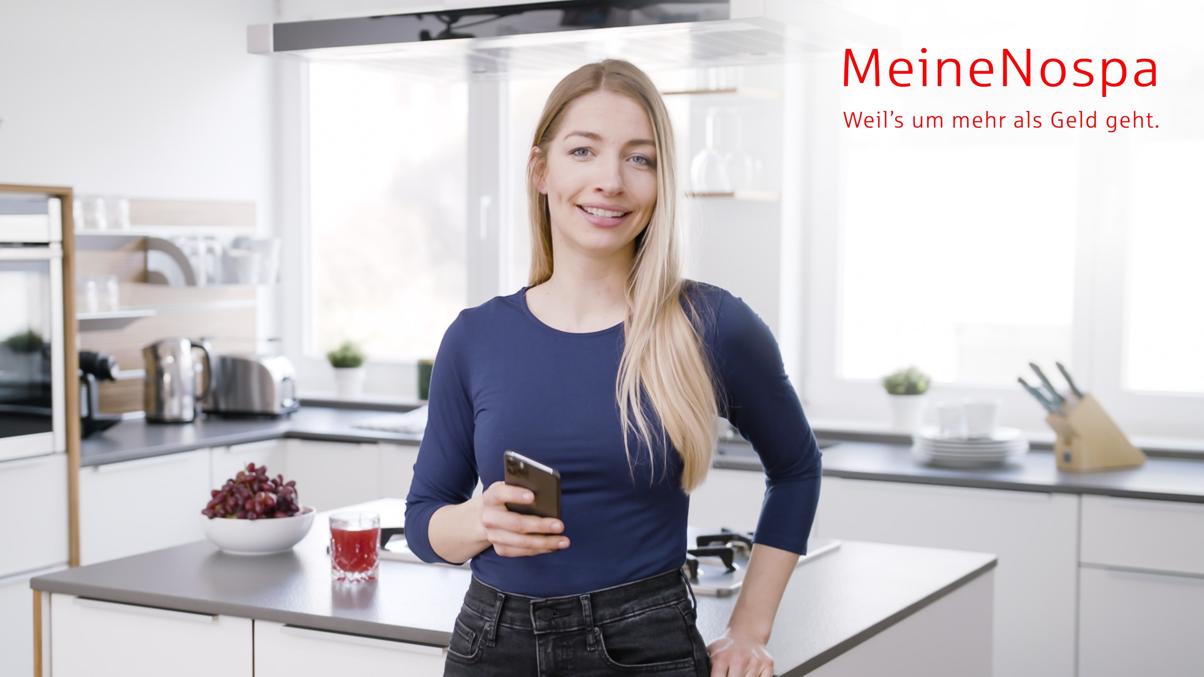 bb_nospa_vorschau.jpg Eine blonde Frau steht in ihrer Küche und lehnt sich an die Kücheninsel