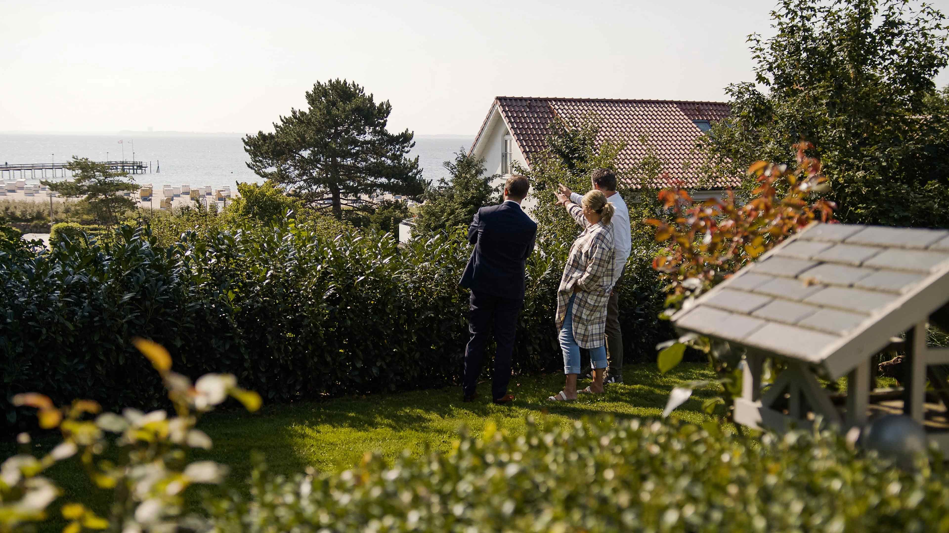 Drei Personen stehen im Garten und zeigen auf das anliegende Meer