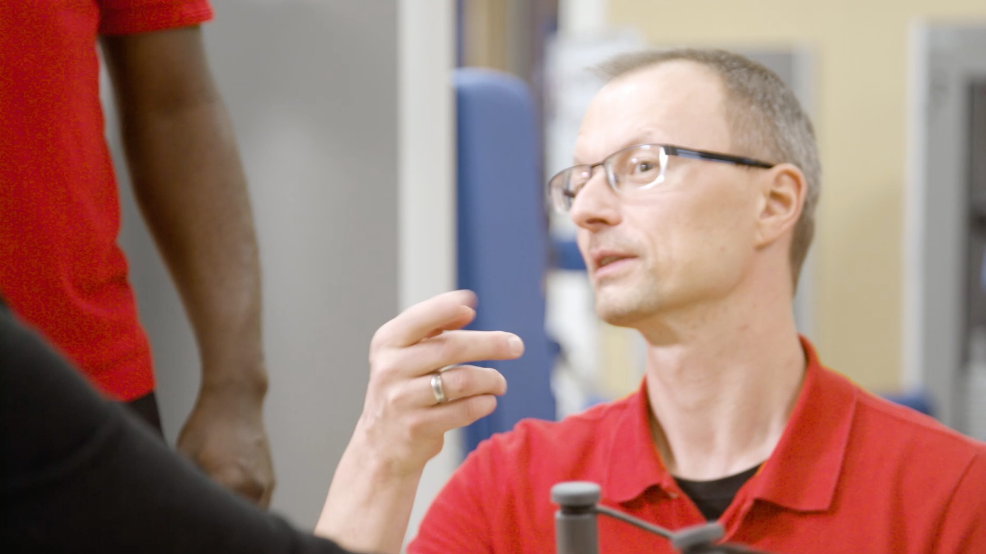 Ein Mann im roten Tshirt und Brille gestikuliert mit der Hand