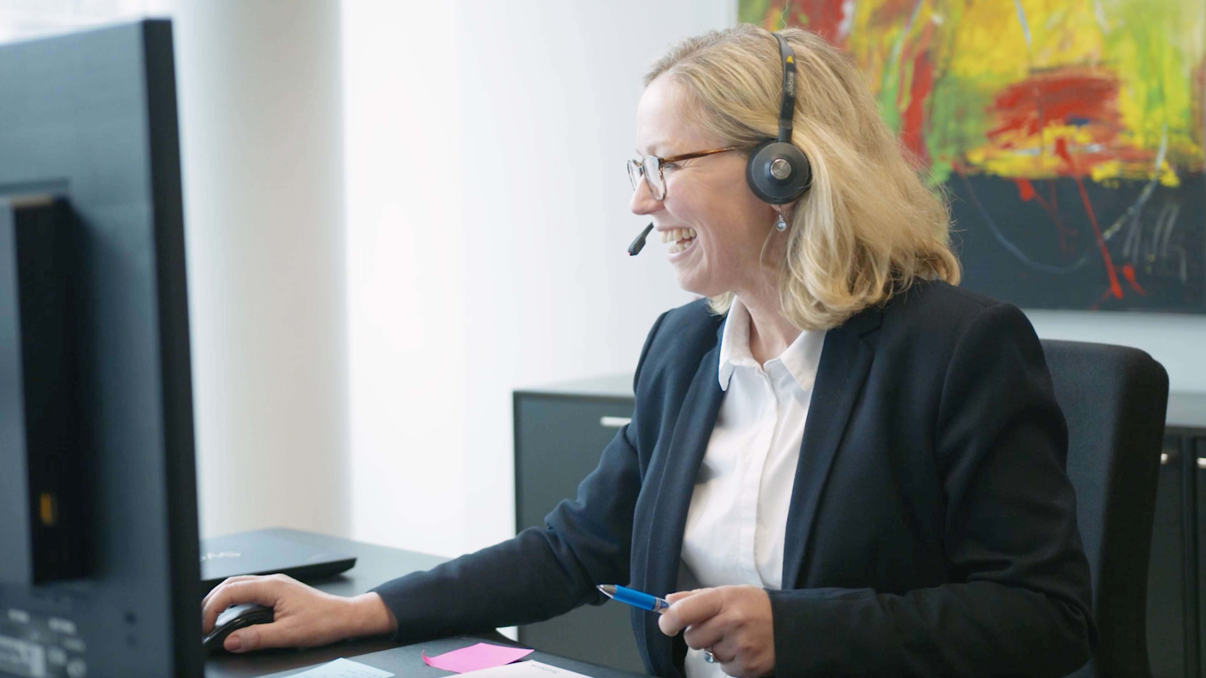 Blonde Frau am Schreibtisch sitzend mit Headset auf dem Kopf